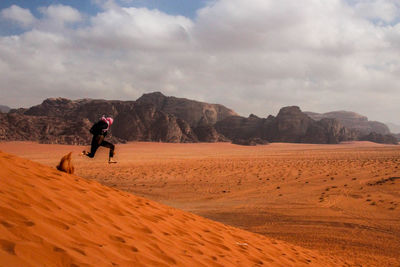 Man on sand dune in desert against sky