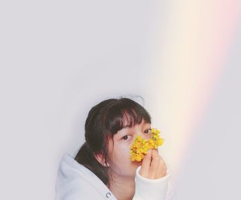 Portrait of woman holding yellow flower against white wall