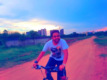 Portrait of man riding bicycle on road against sky