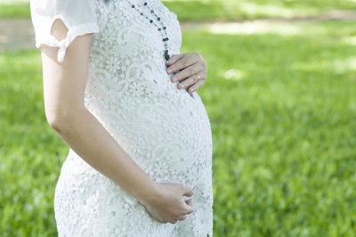 Midsection of pregnant woman with hands on stomach standing in park