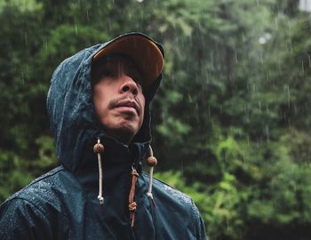 Mature man wearing raincoat standing against trees in forest