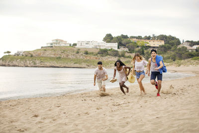 Playful friends running on shore at beach during vacation