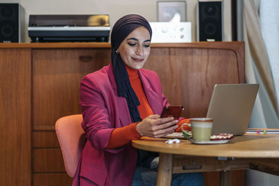 Young woman using mobile phone while sitting on table