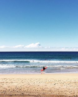 Woman with surfboard walking on shore at beach against sky