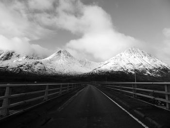 Empty road leading towards snowcapped mountains against sky