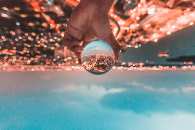 Cropped hand holding crystal ball with reflection of illuminated city against sky during sunset