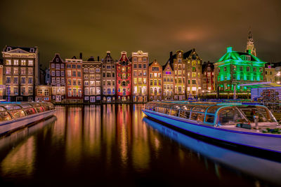 Illuminated buildings by river against sky at night