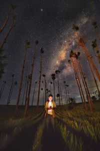 Young man using mobile phone while standing amidst plants on field against star field at night