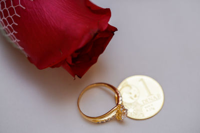High angle view of red rose with diamond ring and gold coin on white background