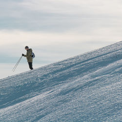 Side view of male hiker hiking on snowcapped mountain against cloudy sky