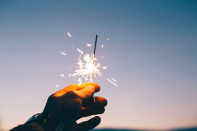 Cropped hand of man holding lit sparkler against sky