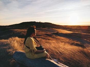 Side view of man sitting on landscape against sunset sky