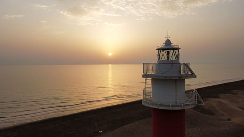 Lighthouse by sea against sky during sunset