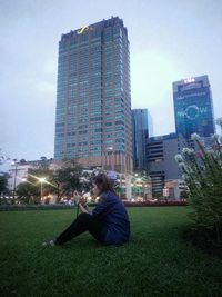 Woman sitting by modern buildings against sky in city