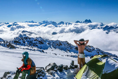 People by tent on snow covered field by mountains against sky