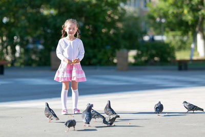 Full length of girl feeding birds on road in city