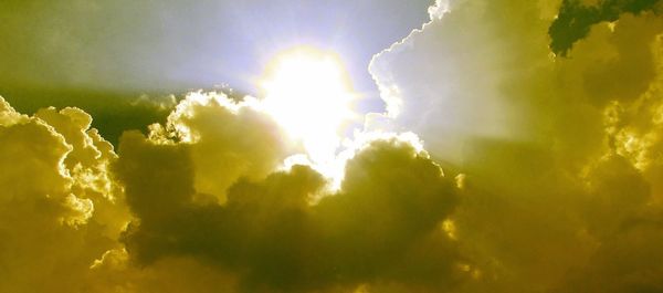Low angle view of sun streaming through clouds in sky