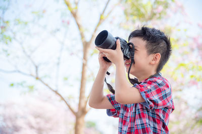 Cute boy photographing with digital camera in park