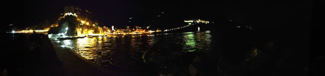 Illuminated city by river against sky at night