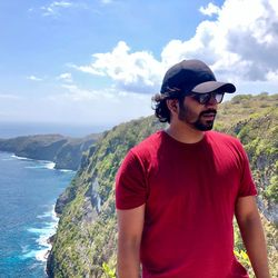 Young man standing on cliff against sky