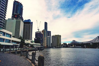 Bridge over river by buildings against sky in city