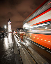Light trails on illuminated city against sky at night