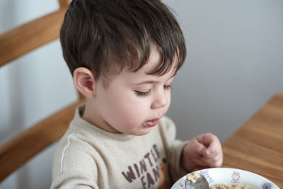 Little boy eating oatmeal for breakfast in the kitchen