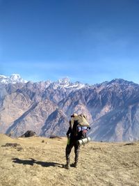 Rear view of person with backpack standing on mountain against blue sky during sunny day