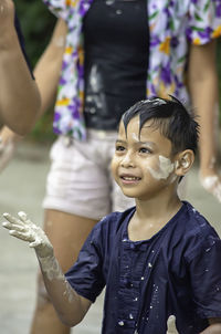 Smiling boy with messy hand and face standing against woman