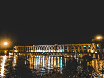 Illuminated buildings by river against clear sky at night