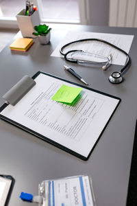 High angle view of clipboard with stethoscope on table at clinic