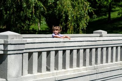 Boy sitting on retaining wall against trees