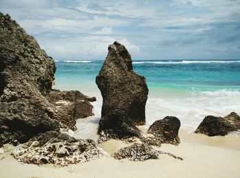 Rocks on beach against cloudy sky