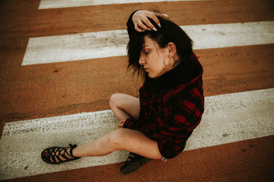 High angle view of young woman sitting on zebra crossing