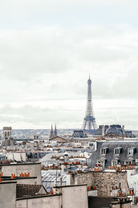 Eiffel tower and buildings in city against cloudy sky