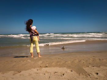 Woman with dog standing on beach against clear sky