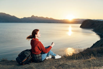 Man sitting in lake against sky during sunset