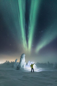 Rear view of man standing on snow against aurora borealis