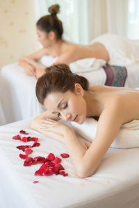 Topless young woman with flower petals lying on massage table in spa