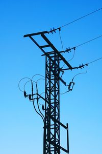 Low angle view of silhouette electricity pylon against blue sky