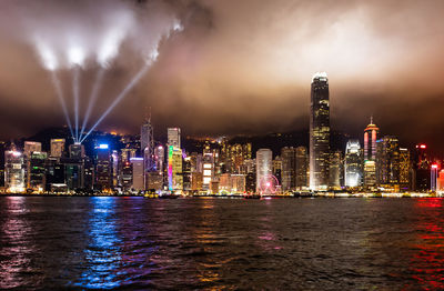 Illuminated buildings by river against sky at night
