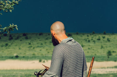 Dramatic photo of summer field before storm. man in chain mail with sword walks across field.