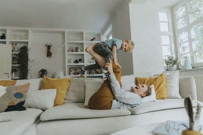 Mother picking son on leg while playing on sofa at home