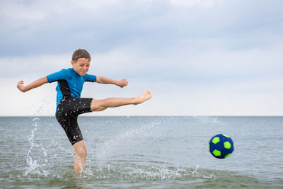 Full length of boy playing soccer ball in water at beach