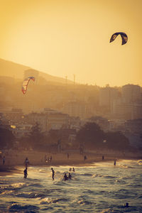 People enjoying at beach against sky during sunset