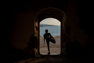 Woman exercising on doorway against sea during sunset
