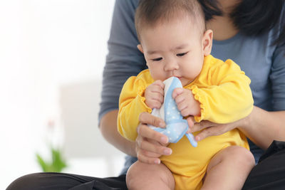 Loving mother putting shoes on baby on sofa at home