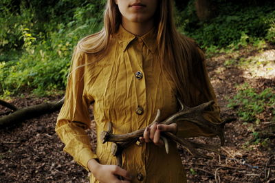 Midsection of woman holding antler while standing in forest