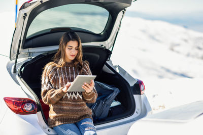 Young woman using digital tablet standing by car during winter outdoors