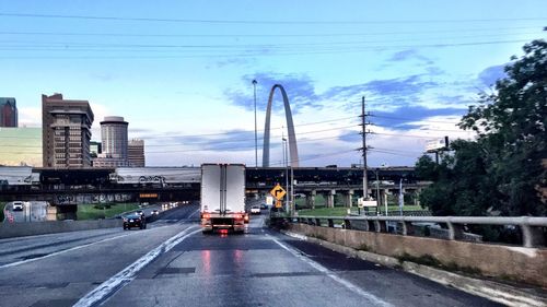 Cars moving on illuminated city against blue sky